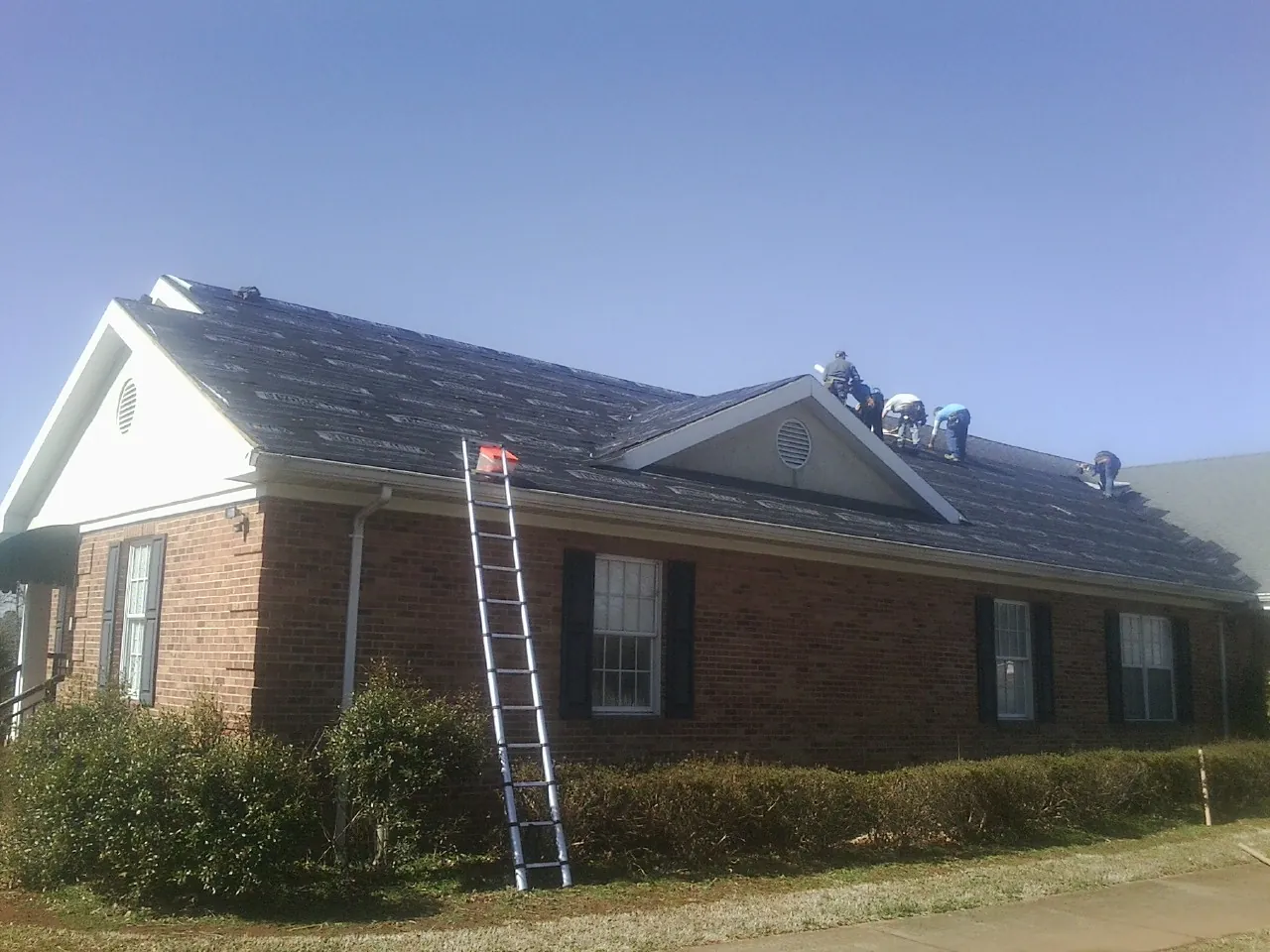 Crew tearing shingles off a brick ranch roof with a ladder set — Metal Roof Repair work by our crew in New York