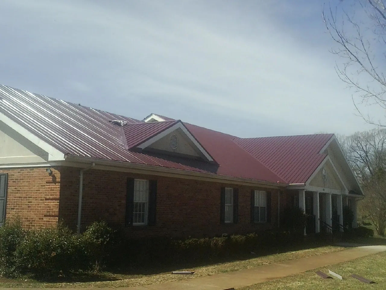Red metal roof with gabled entries on a long brick building, from a Hail Damage Roof Repair job in New York
