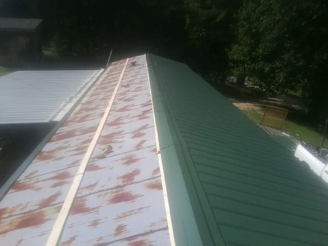 Old rusted panels beside newly installed green metal roofing — Wind Damage Roof Repair by Roofing Brothers in New York