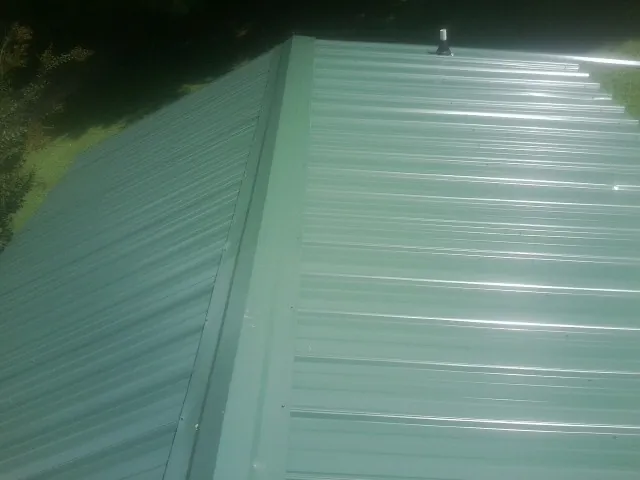 New green metal panels meeting at the ridge of a roof — Flat Roof Repair work by our crew in New York
