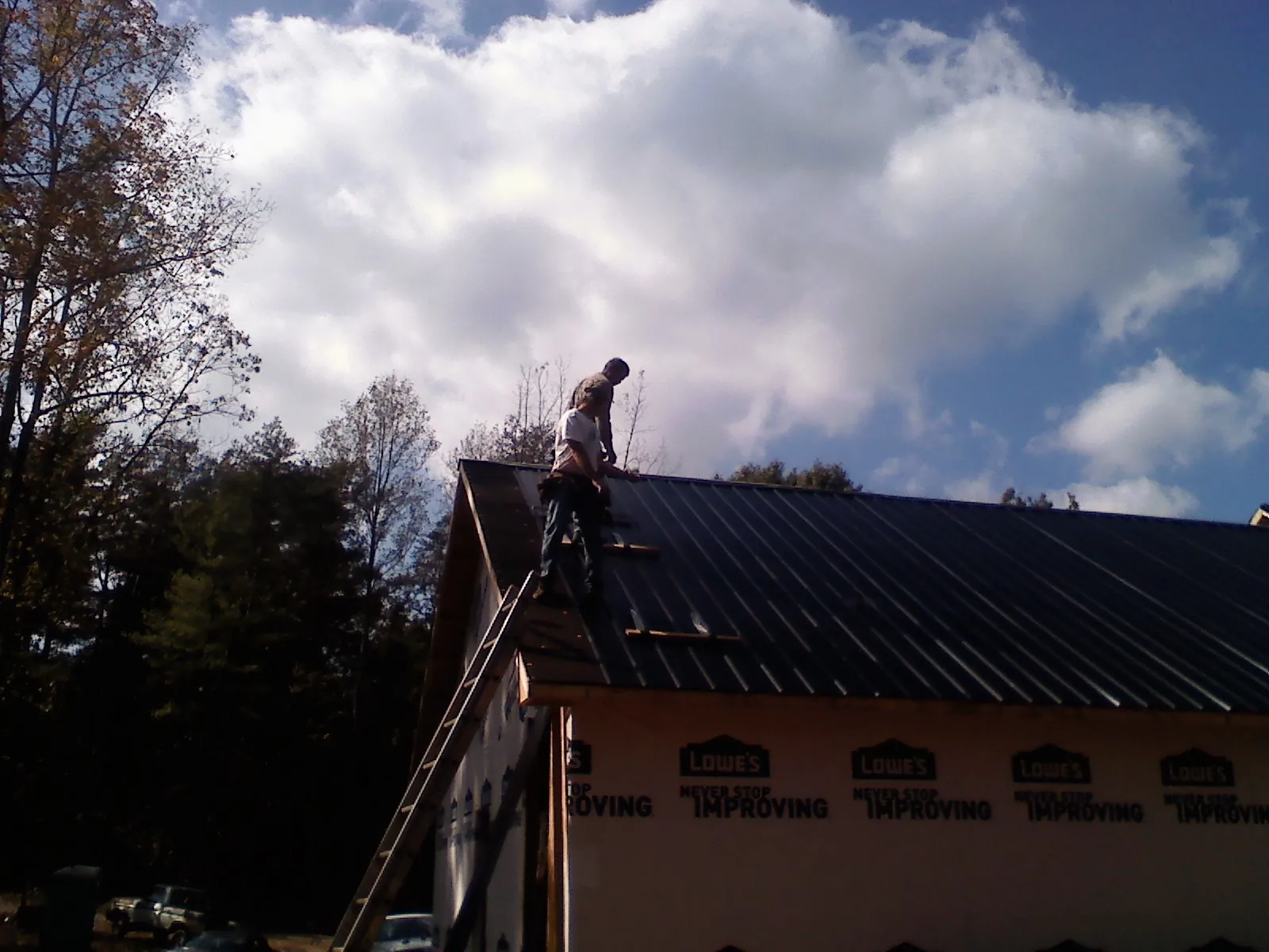 Roofer fastening dark metal panels high against a cloudy sky, from a Roof Inspection job in New York