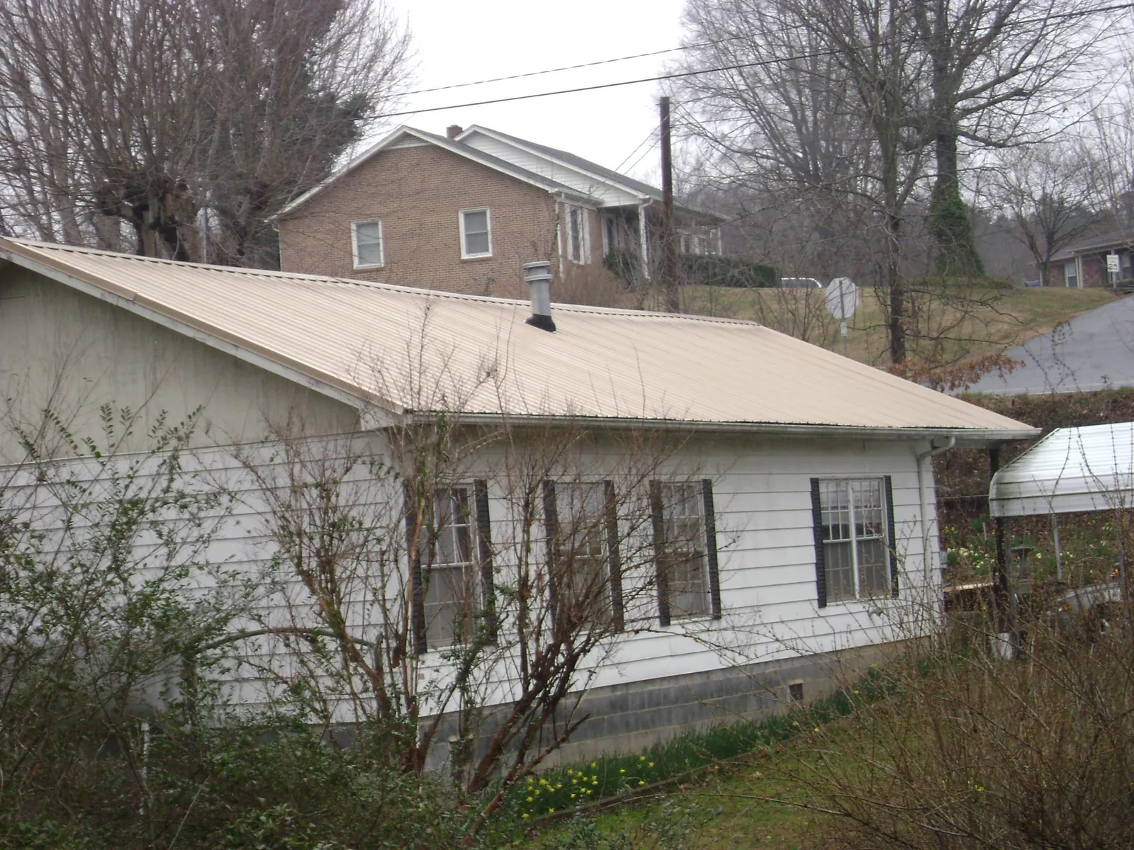Tan metal roof on a white sided house set into a hillside — Commercial Roofing by Roofing Brothers in New York